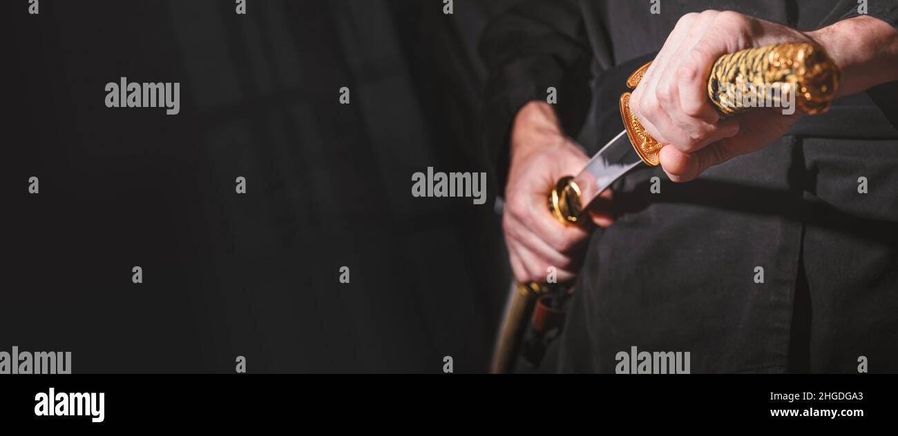 Der Samurai hält ein japanisches Katana-Schwert, Banner. Foto eines Kriegers in schwarzer Kleidung in niedriger Tonart mit Platz für Text Stockfoto