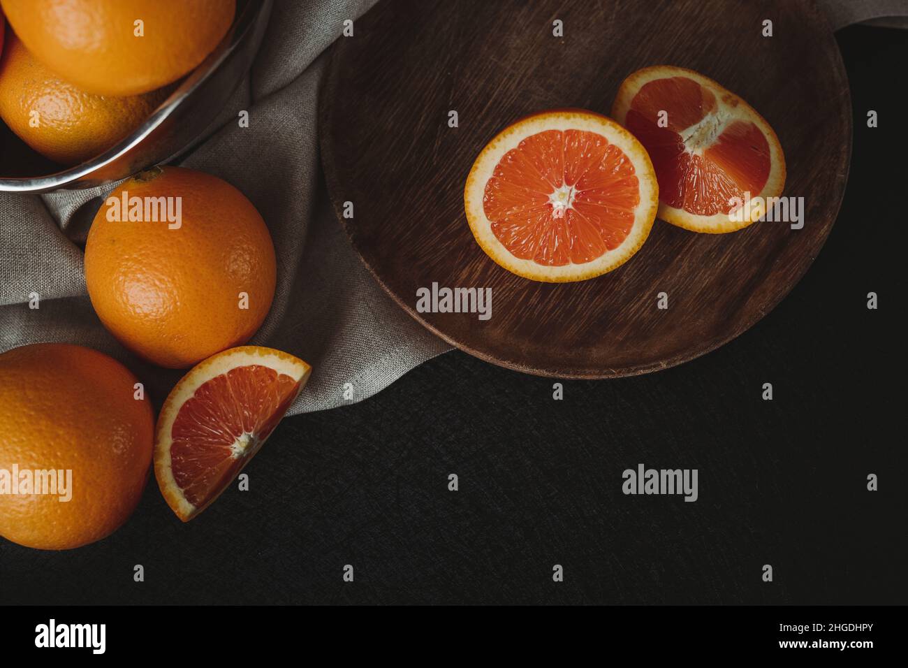 Moody Citrus Flat Lay mit Copy Space. Cara Cara Orangen auf dunklem Hintergrund. Orangefarbene Scheiben auf Holzplatte. Dunkle Winterästhetik. Stillleben. Stockfoto