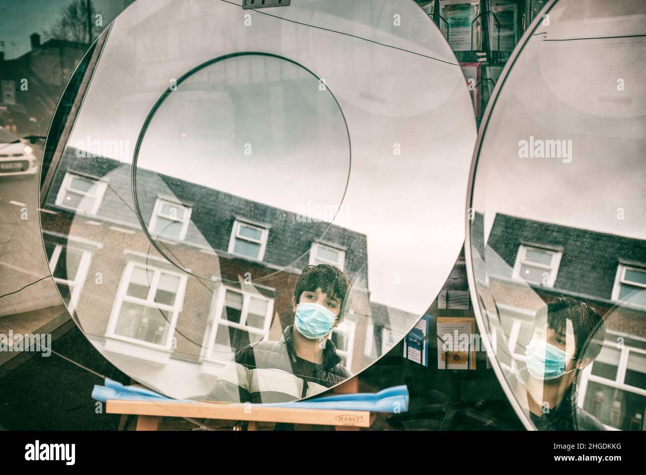 Teenager, der eine Gesichtsmaske trägt, sieht seine Spiegelung im Schaufensterspiegel in London, Großbritannien Stockfoto