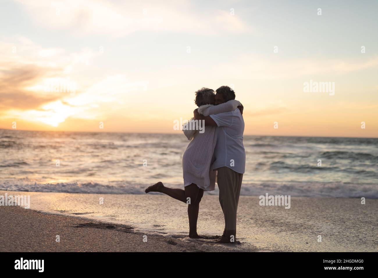 Seitenansicht eines mehrrassigen älteren Ehepaares, das sich während des Sonnenuntergangs am Strand umarmte und küsste Stockfoto