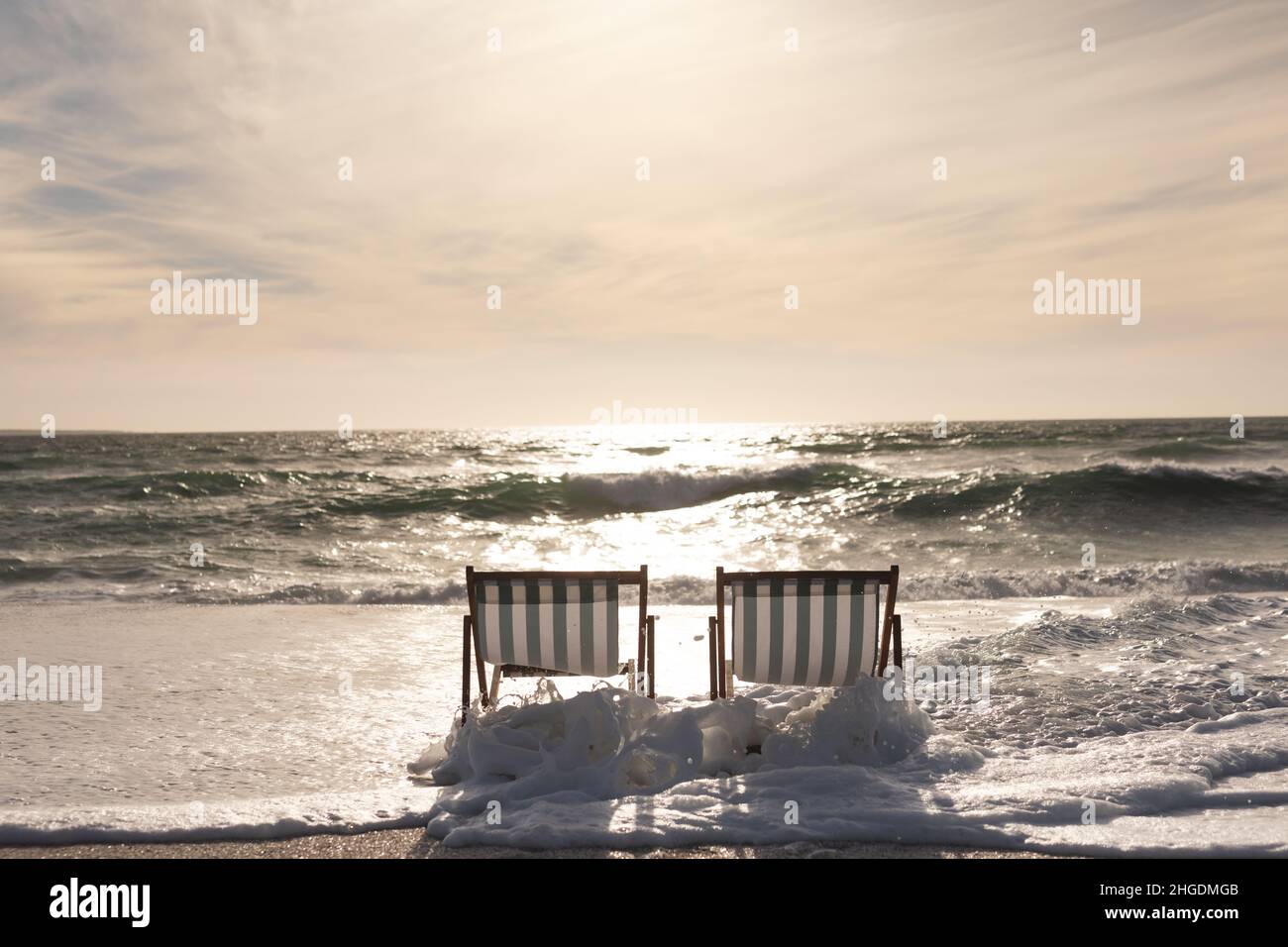 Wackeln Sie auf leeren zwei klappbaren Holzstühlen am Strand gegen den Himmel während des Sonnenuntergangs Stockfoto