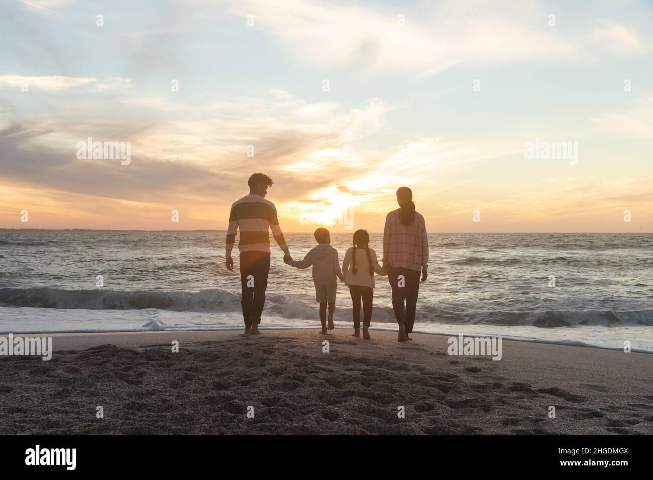 Rückansicht einer multirassischen Familie, die während des Sonnenuntergangs zum Strand läuft Stockfoto