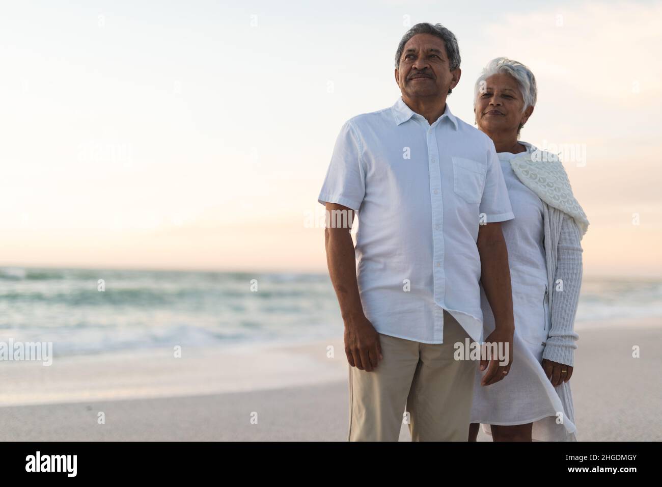 Nachdenkliche ältere, multirassische Männer und Frauen, die während des Sonnenuntergangs vom Strand zum Himmel blicken Stockfoto