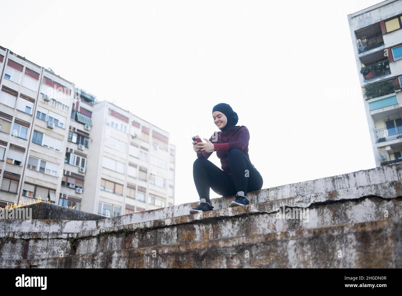 Junge muslimische Frau, die während ihres Trainings im Freien eine Telefonpause einlegen musste Stockfoto