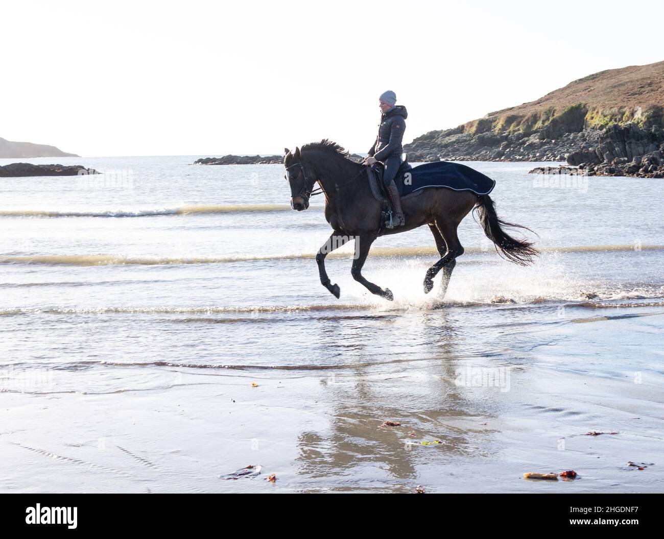 Silhouette einer Frau, die am Strand auf dem Pferd durch Wellen reitet. West Cork Irland Stockfoto