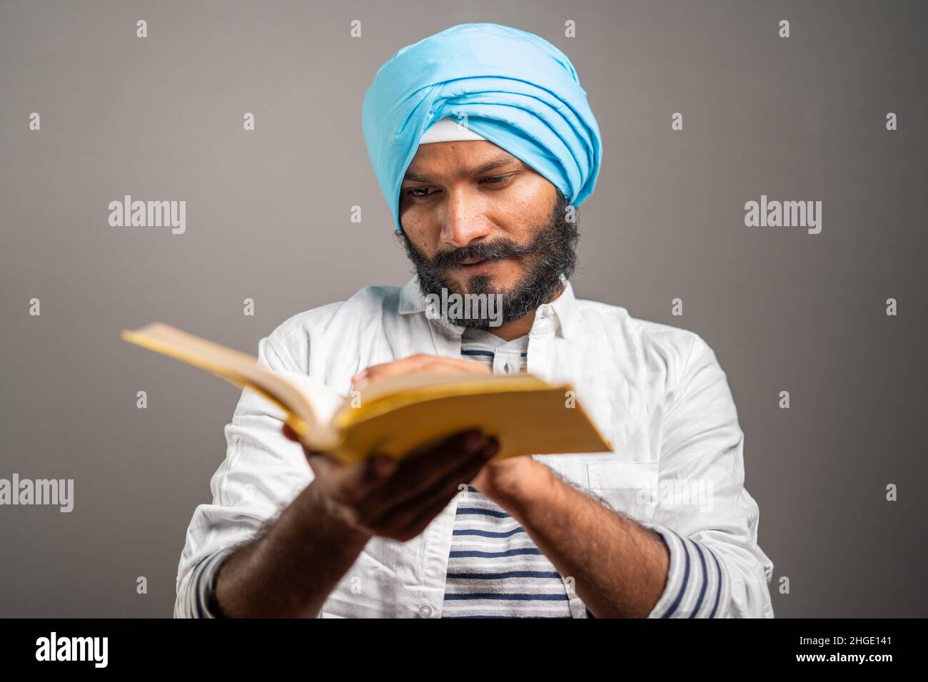 Junger sikh-Mann, der die heilige religiöse Schrift liest, um Gott auf grauem Hintergrund zu beten - Konzept von spirituellen Lügen, Anbetung und traditioneller Kultur. Stockfoto