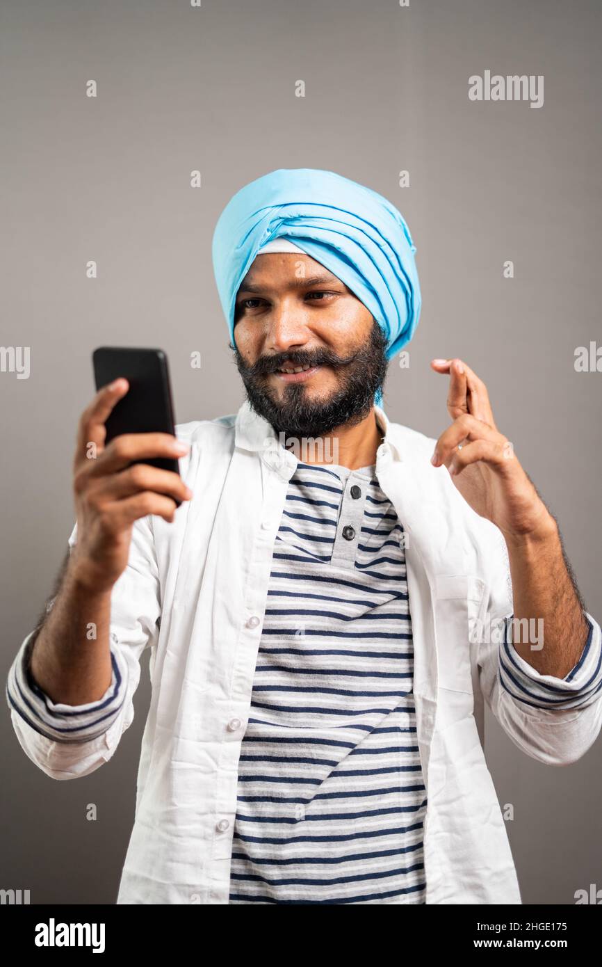 Konzept des Watens für die Jobförderung, Lotterie oder Interview-Ergebnisse zeigen von angespanntem jungen sikh Mann mit Handy auf Studio-Hintergrund. Stockfoto