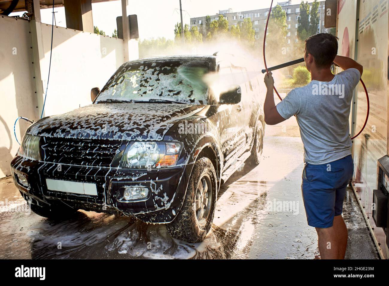 Ein schwarzer SUV-Wagen bei einer Autowaschanlage zur Selbstbedienung. Waschen Sie das Auto mit Ihren eigenen Händen. Ein schwarzes Auto in Reinigungsschaum. Ein Mann wäscht tagsüber sein Auto. Stockfoto