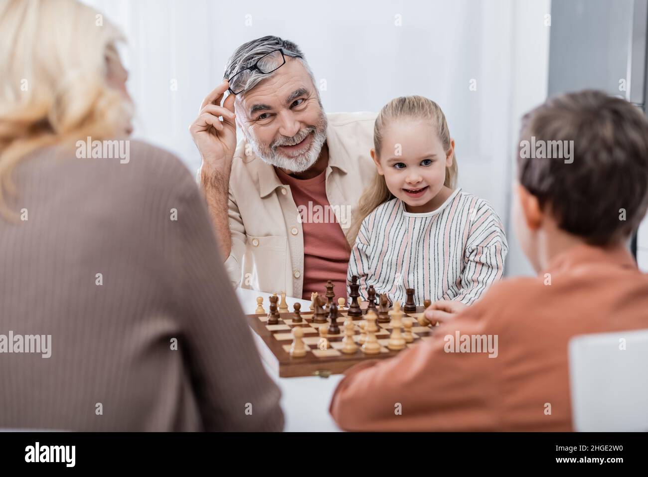 Lächelnder Mann mit Brillen, während er mit Frau und Enkelkindern Schach spielt Stockfoto