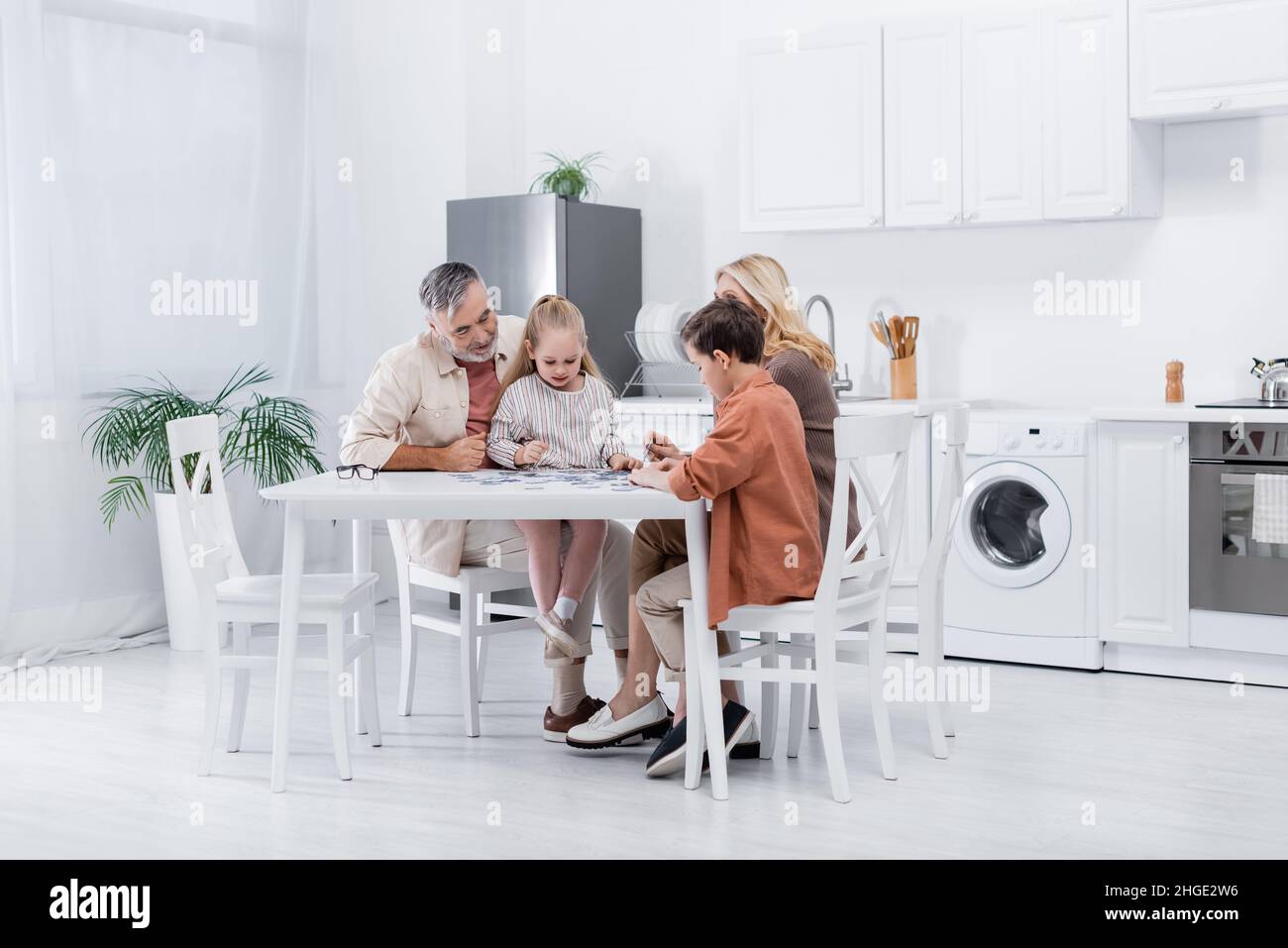 Großeltern mit Enkeln spielen Puzzle-Spiel in der modernen Küche Stockfoto