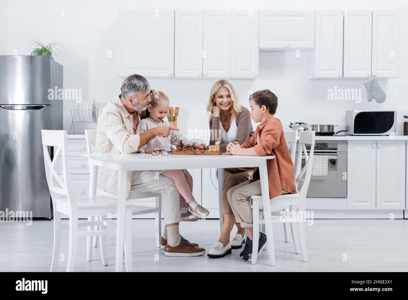 Älterer Mann zeigt mit dem Finger, während er mit Frau und Enkeln Schach spielt Stockfoto