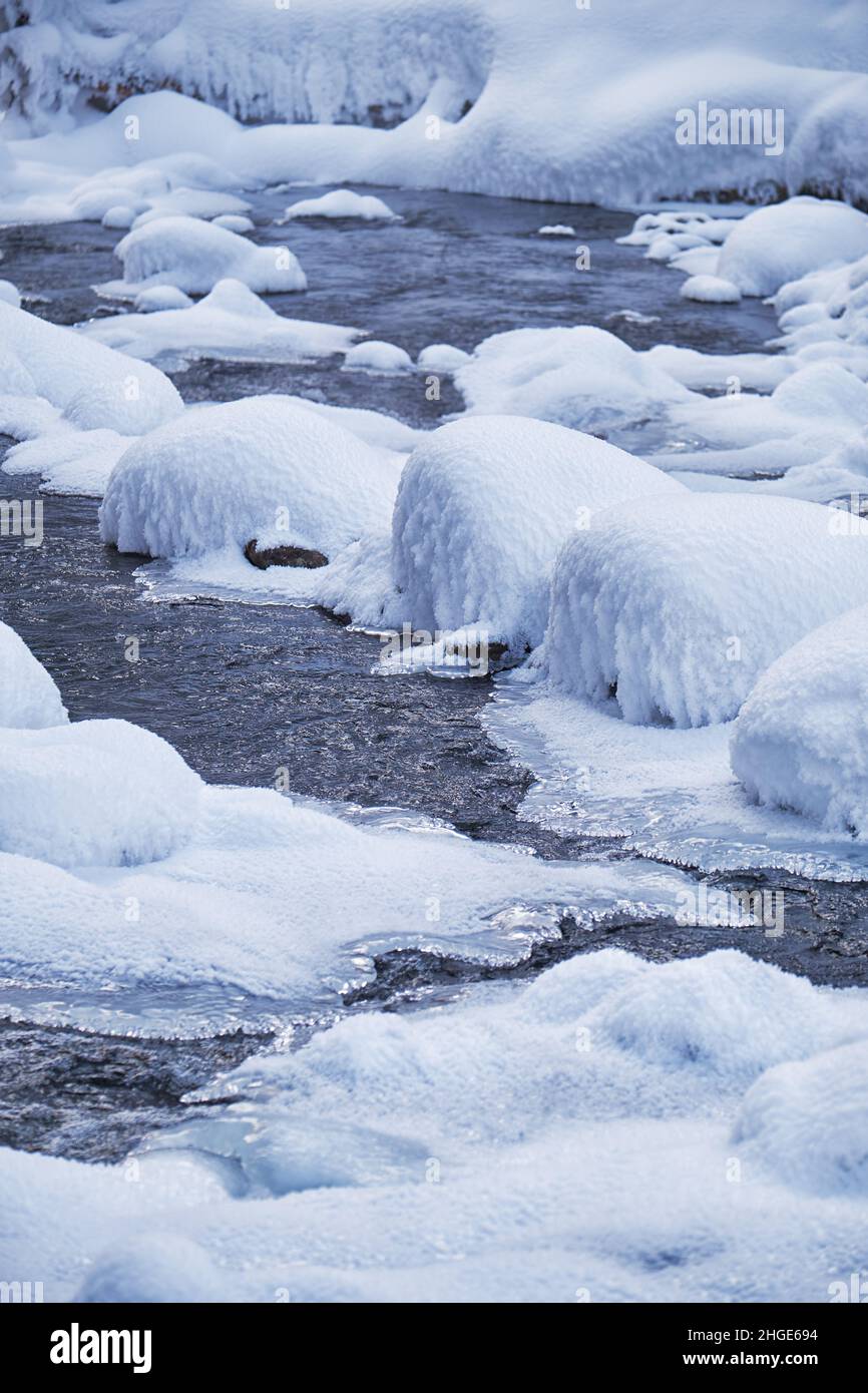Foto von Steinen mit Schneekappen und Eis im Wasser des gefrorenen Flusses Pescherka in der Nähe von Wasserfall in der Wintersaison. Sibirien, Russland Stockfoto