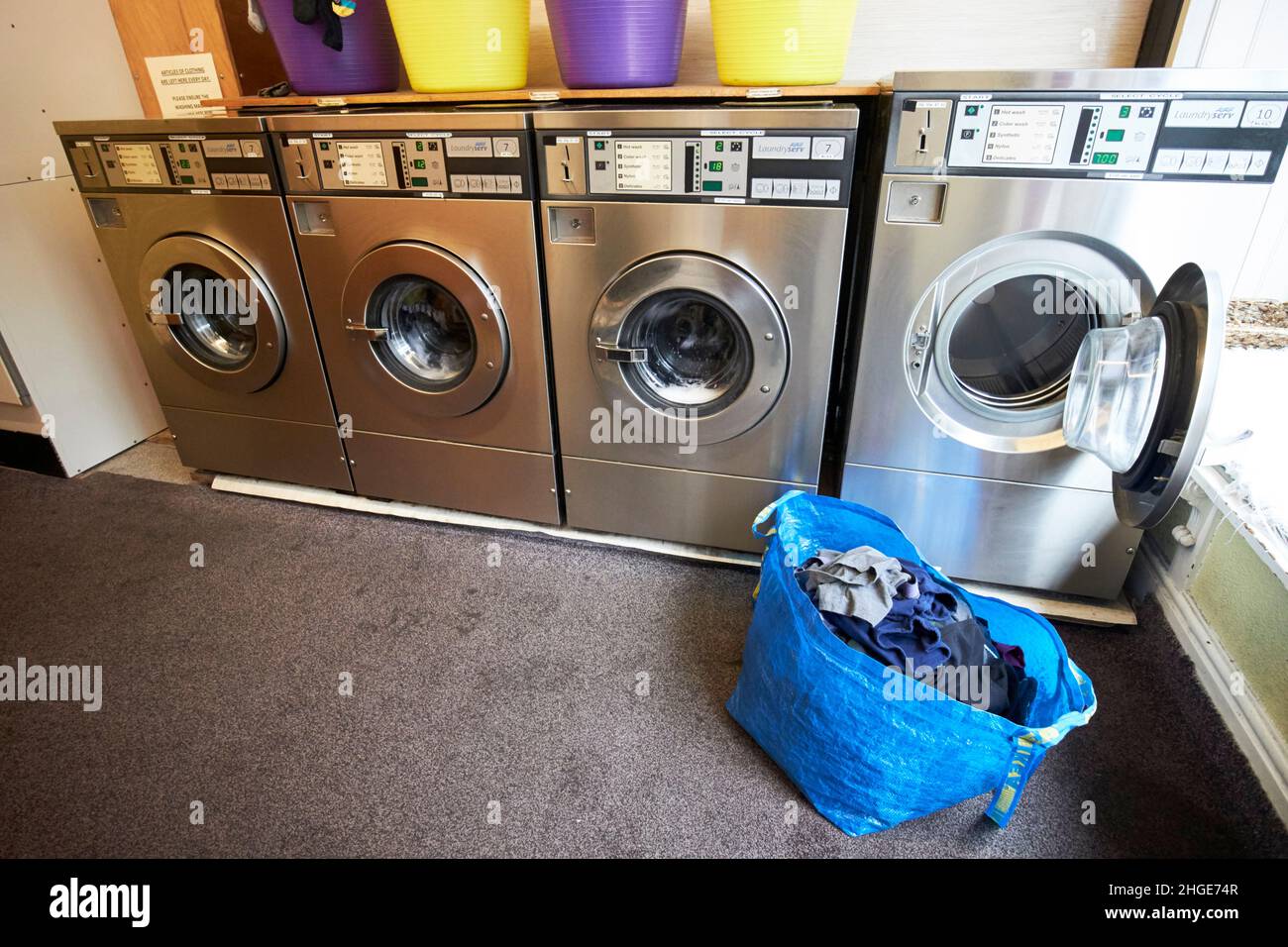 Beutel mit sauberer Wäsche und offener Waschmaschine in Reihe von Waschmaschinen in einem Waschsalon in ambleside Lake District, cumbria, england, großbritannien Stockfoto