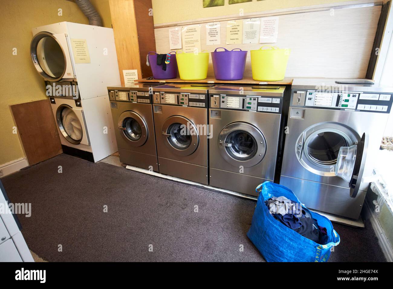 Beutel mit sauberer Wäsche und offener Waschmaschine in Reihe von Waschmaschinen in einem Waschsalon in ambleside Lake District, cumbria, england, großbritannien Stockfoto