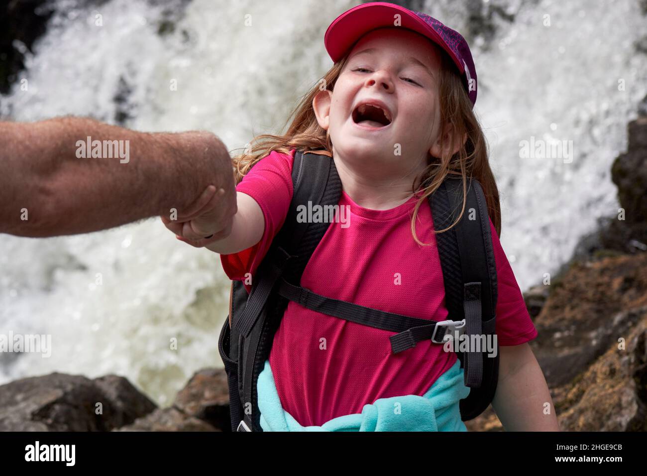 Das junge Mädchen, das vorgibt, in einen Wasserfall zu fallen, wird von ihrem Väter Arm Lake District, cumbria, england, großbritannien, gehalten Stockfoto
