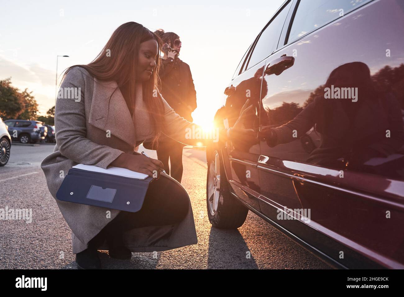 Versicherungsvertreter untersucht das Auto, während der Fahrer auf dem Mobiltelefon spricht. Unfallanspruchsprozess. Afroamerikanische Frau, die den Schaden an der überprüft Stockfoto