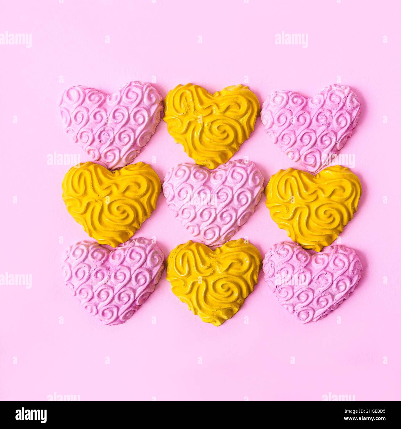 Vier gelbe und fünf rosa Herzen, die in einem Quadrat auf pastellrosa Hintergrund angeordnet sind. Minimalistisches romantisches Konzept für Valentinstag-Feier-Banner oder -Karte. Stockfoto