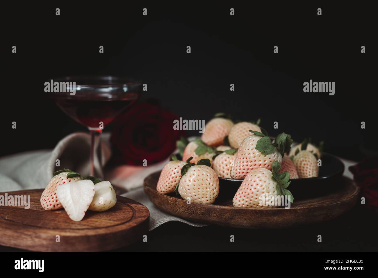 Moody Valentine Still Life. Pineberry auf Holzplatte mit dunklem Hintergrund. Weiße Erdbeere. Dunkle Valentinsästhetik. Erdbeeren und Wein. Stockfoto