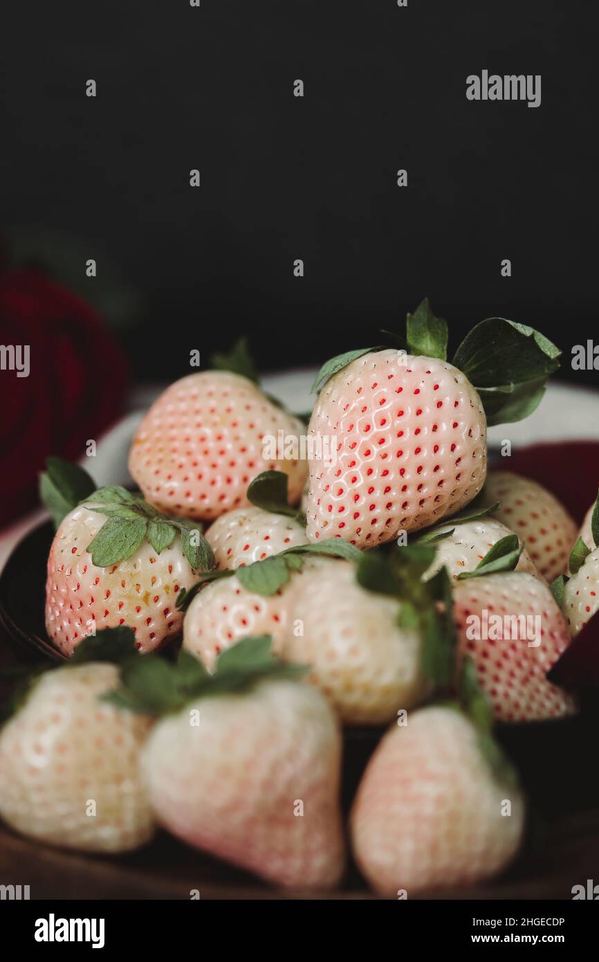 Moody Valentine Still Life. Pineberry auf Holzplatte mit dunklem Hintergrund. Weiße Erdbeere. Dunkle Valentinsästhetik. Erdbeeren und Wein. Stockfoto