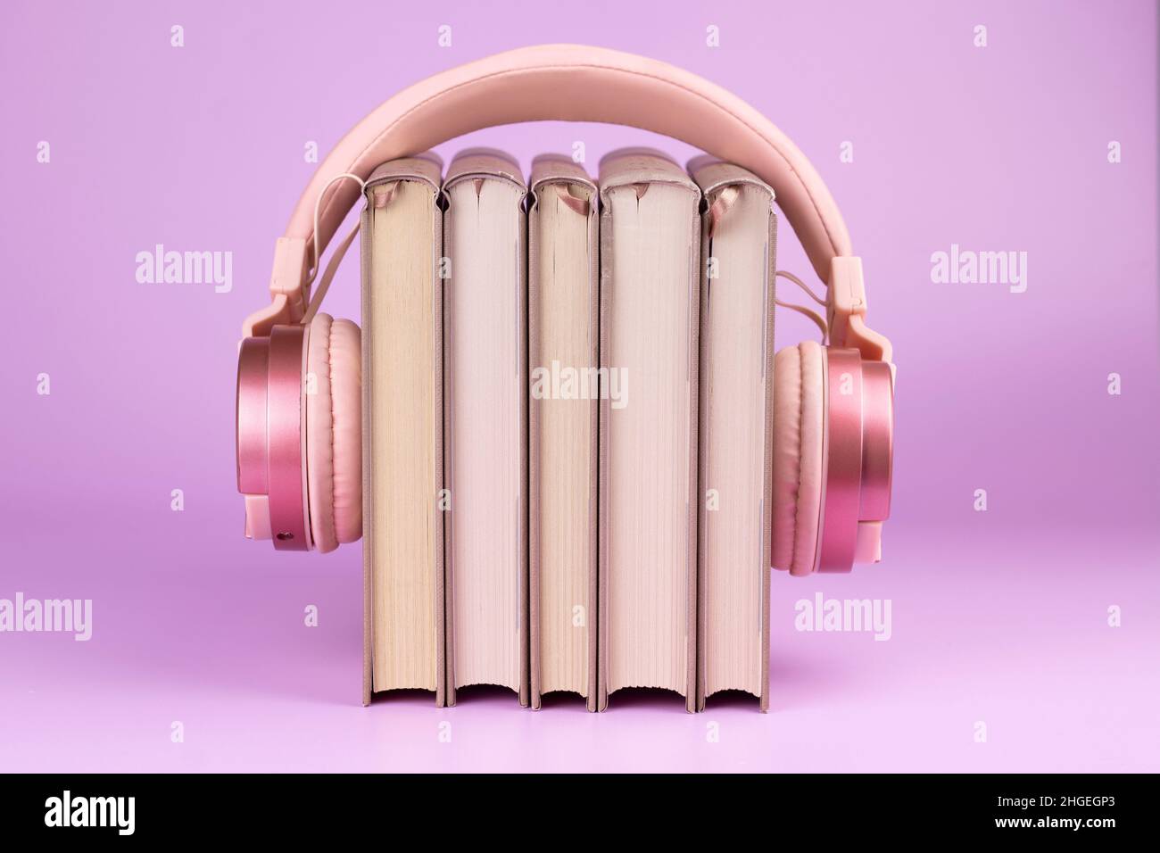 Kopfhörer und Bücherstapel auf rosa Hintergrund. Konzept des Hörbuchs. Stockfoto