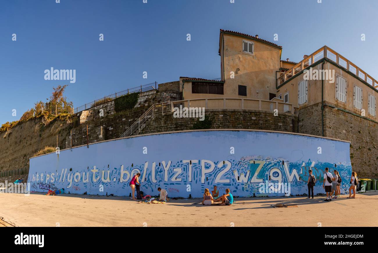 Ein Bild von einem Graffiti, das einen verkürzten YouTube-Link am Strand von Piran zeigt. Stockfoto