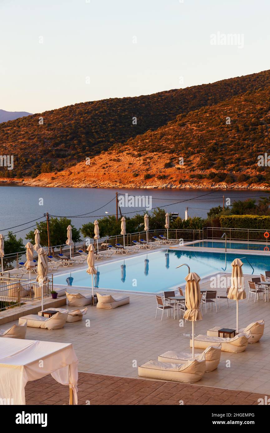 Luxuriöser Swimmingpool am Morgen mit leeren Liegestühlen, Tischen und Sonnenschirmen im Resort mit wunderschönem Meerblick. Griechische Insel Stockfoto
