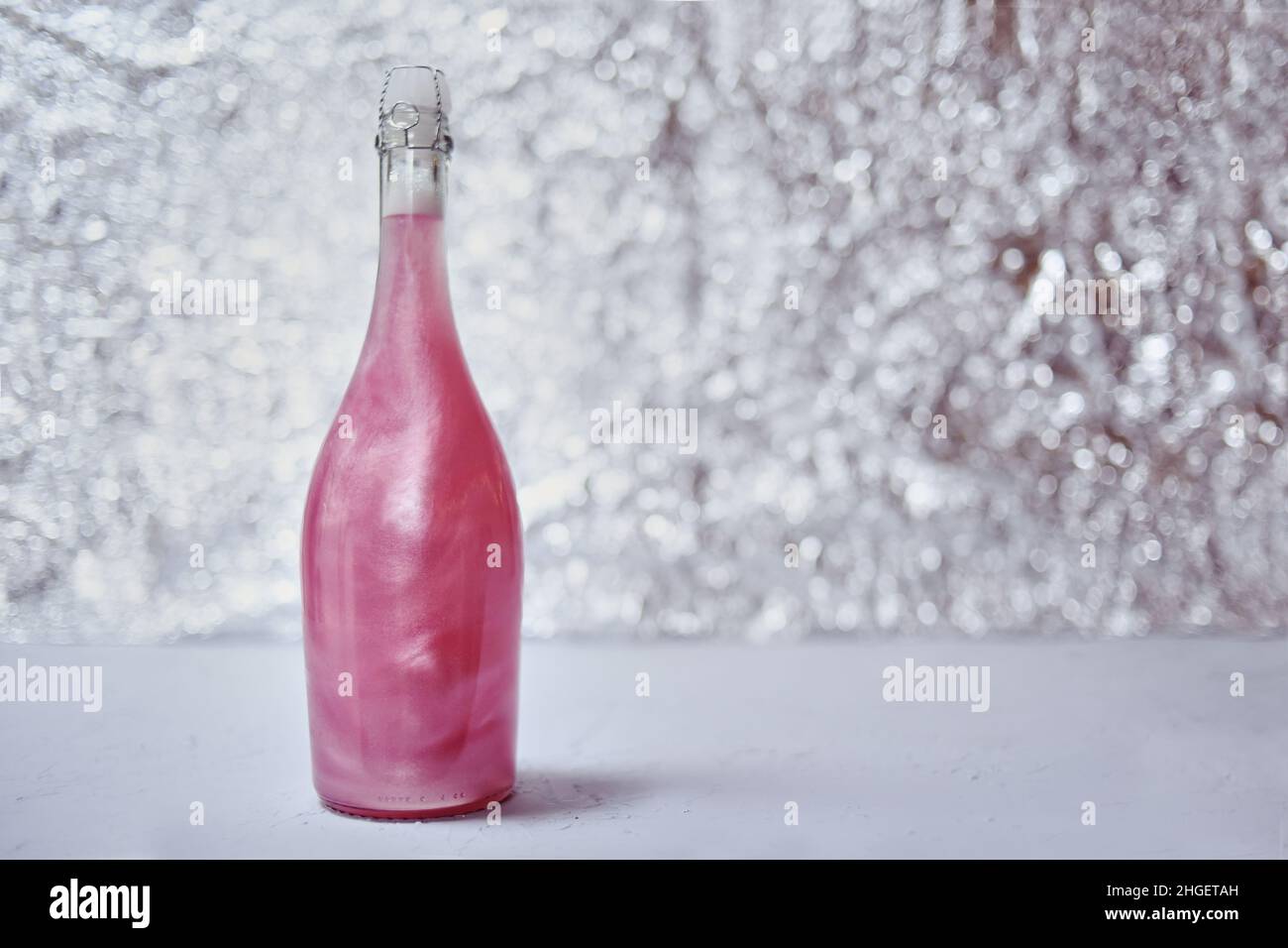 Farbiger Champagner auf glänzendem Hintergrund. Champagnerrosa Rose mit funkelnden Reflexen auf einem Bokeh-Hintergrund. Stockfoto