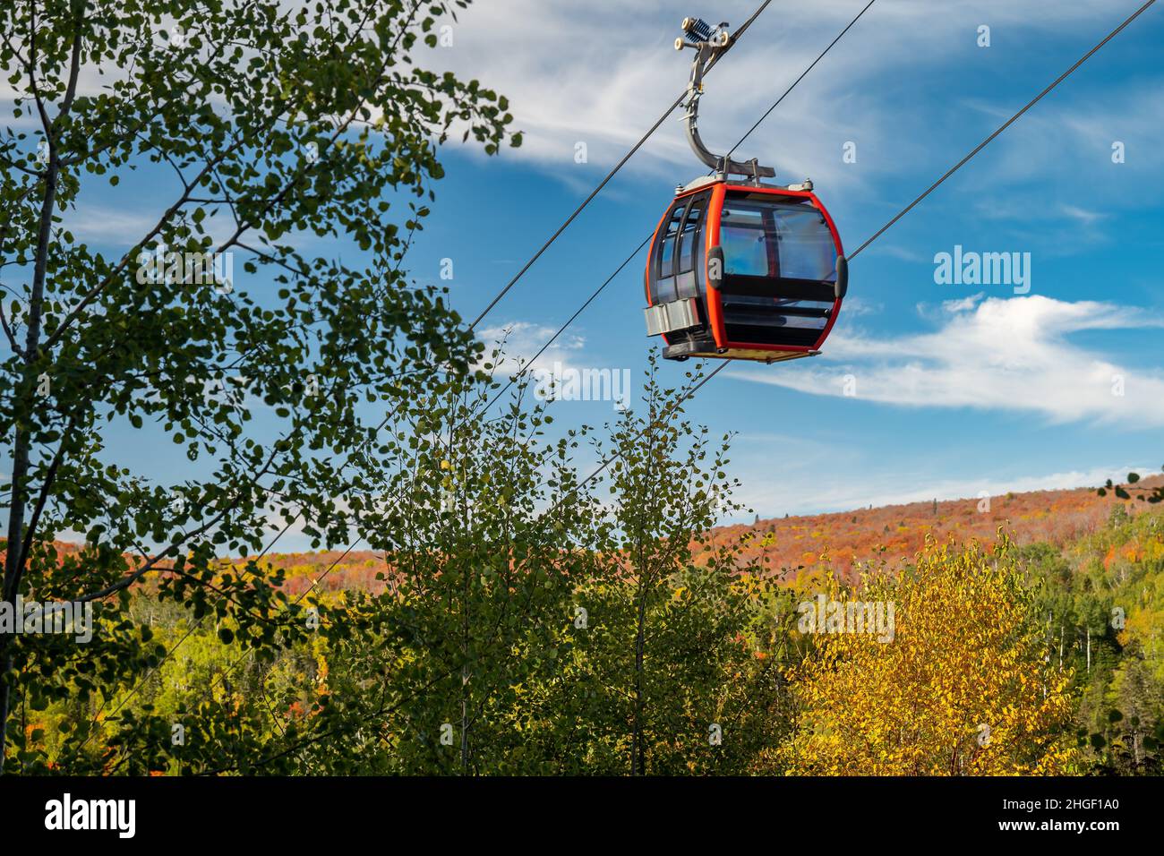 Die Seilbahn auf einer Seilbahn führt an nahe gelegenen Bäumen an einem Skihang in Minnesota vorbei, mit Herbstfarben auf dem fernen Hügel und meist blauem Himmel. Stockfoto