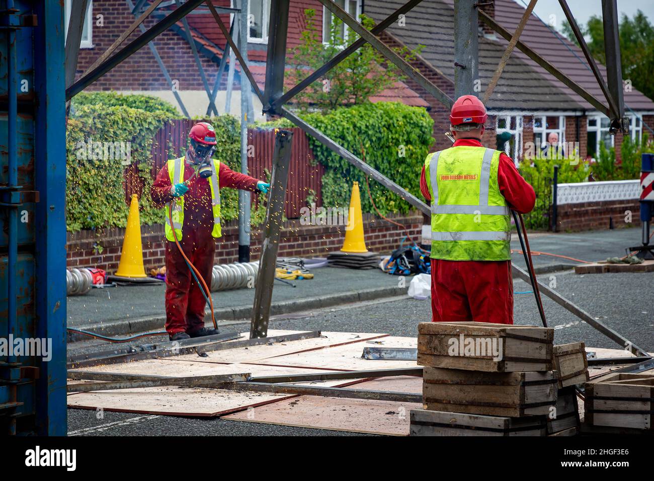 Arbeiter in PSA verwenden oxyde Acetylenbrenner, um beschädigte Teile eines geerdeten Strommasylons auszuschneiden Stockfoto