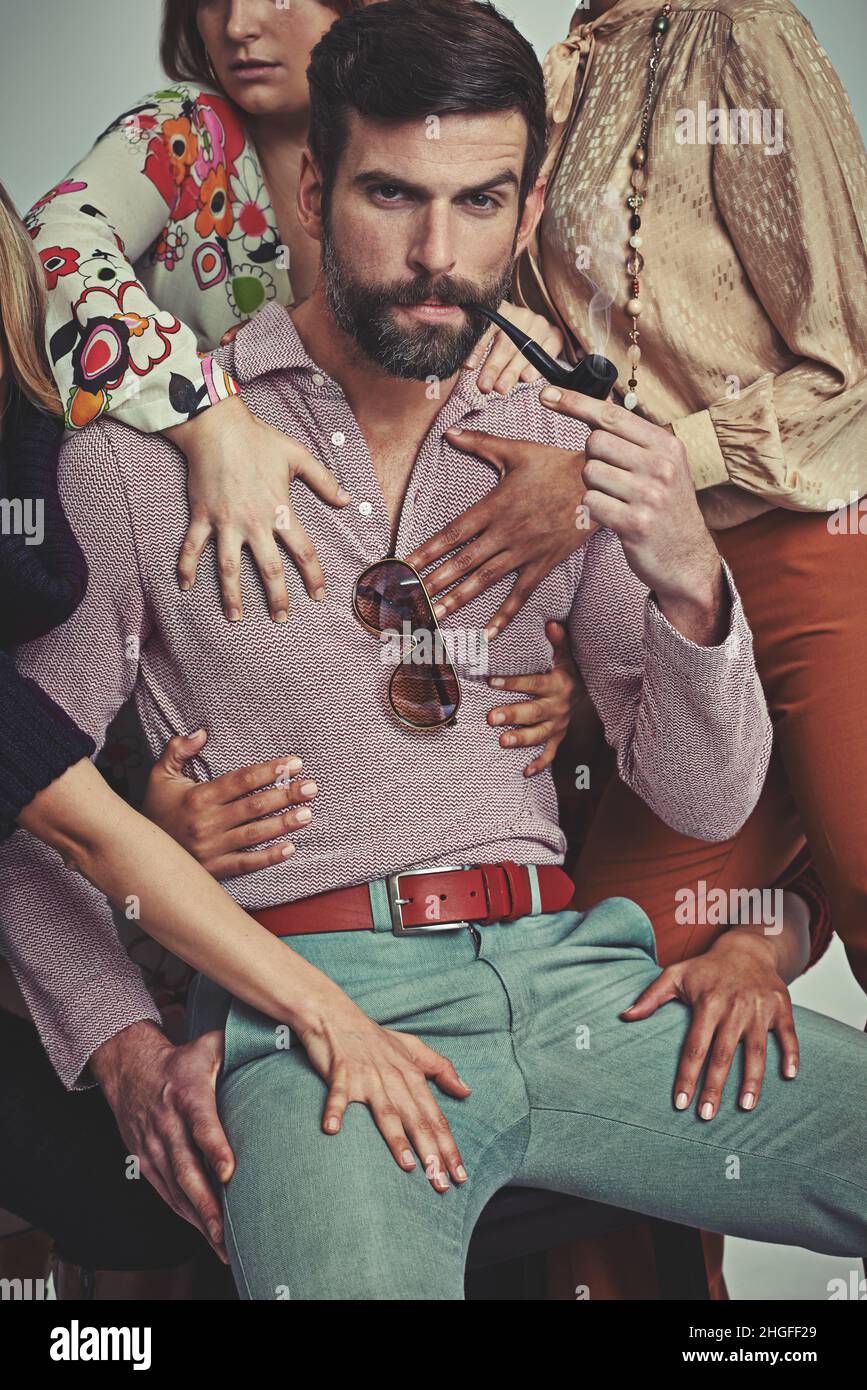 Ich bin ein Mann, ganz sicher. Studioaufnahme eines attraktiven Mannes im Retro-Stil von 70s, der von Frauen berührt wird, während er seine Pfeife raucht. Stockfoto