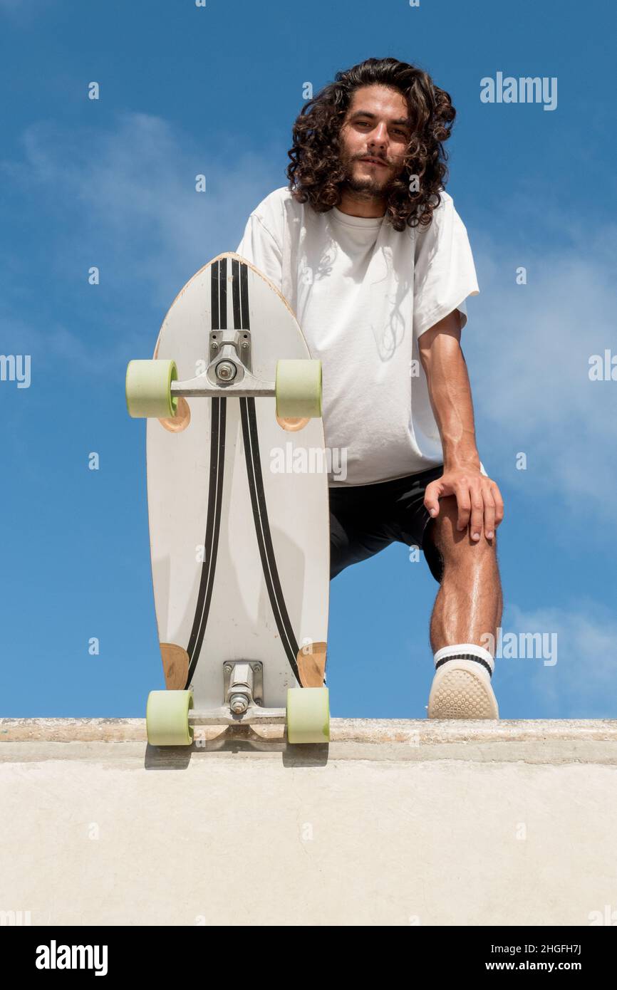 Junge attraktive Skater Porträt Blick auf die Kamera. Er hat lange schwarze Haare und einen Bart. Stockfoto