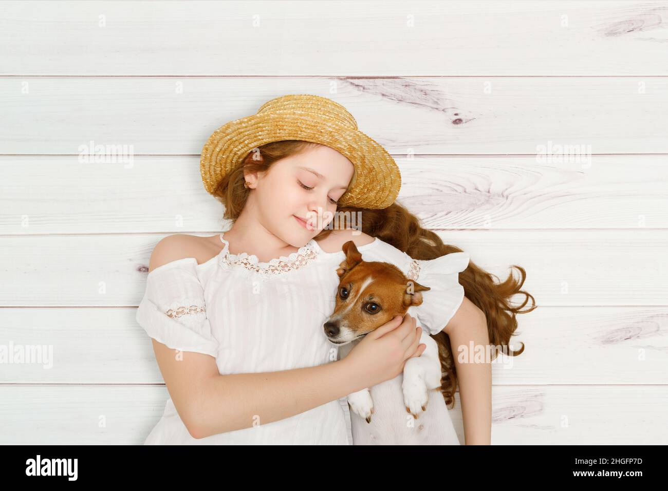 Das kleine Mädchen umarmt ihren Hund, der auf einem Holzboden liegt. Stockfoto