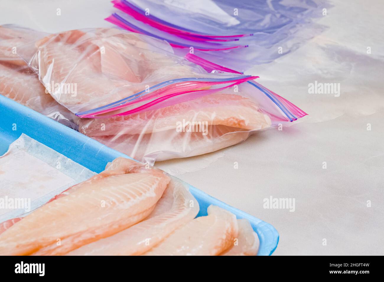Frisches rohes Fischfilet in Reißverschlussbeuteln. Tilapia Filet auf hellem Marmorhintergrund, Nahaufnahme Stockfoto