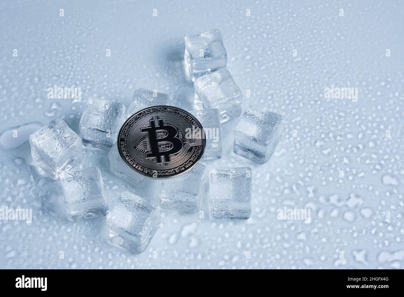 Bitcoin Münze Mitte schmelzende Eiswürfel und Wassertropfen auf hellem Hintergrund Stockfoto