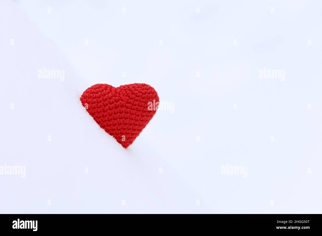 Rot gestricktes Herz im Schnee. Hintergrund für Valentinskarte, romantische Liebe Stockfoto