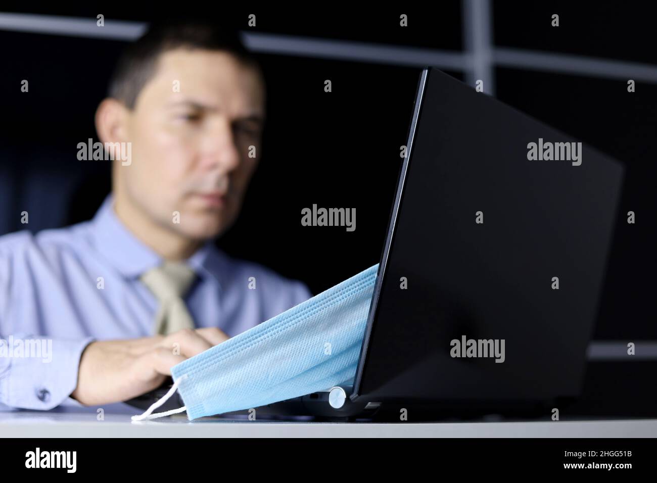 Entfernt Gesichtsmaske auf dem Hintergrund des Mannes in Bürokleidung am Laptop-Display sitzen. Sicherheit während einer Coronavirus-Pandemie Stockfoto