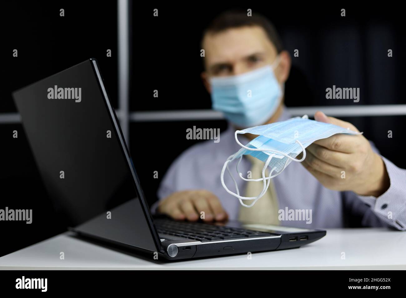 Mann in Bürokleidung, der eine Packung mit schützenden Gesichtsmasken am Laptop-Display trägt. Sicherheit am Arbeitsplatz während einer Coronavirus-Pandemie Stockfoto