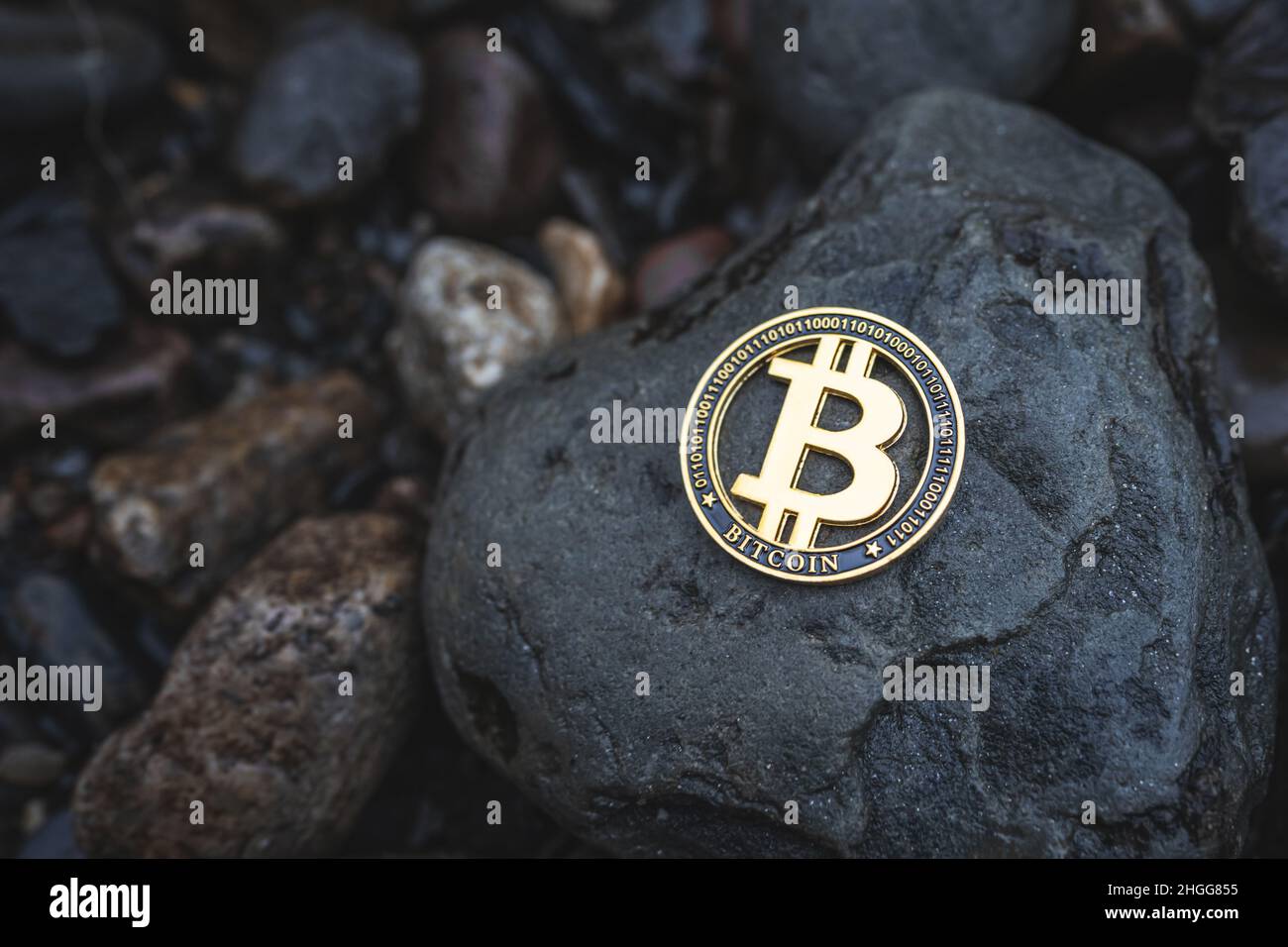 Bitcoin Krypto-Münze mit Platz für Text. Nahaufnahme einer einzelnen Gold-BTC-Kryptowährung auf Felsen im Freien. Foto mit niedriger Tonart für Banner und Nachrichten. Stockfoto