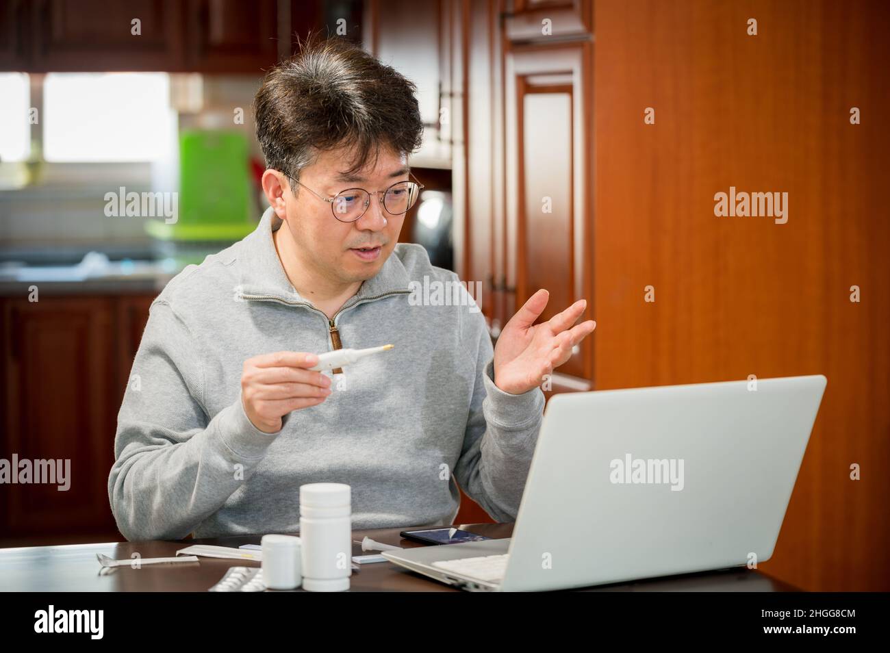 Asiatischer Mann mittleren Alters, der zu Hause Telemedizin erhält. Stockfoto
