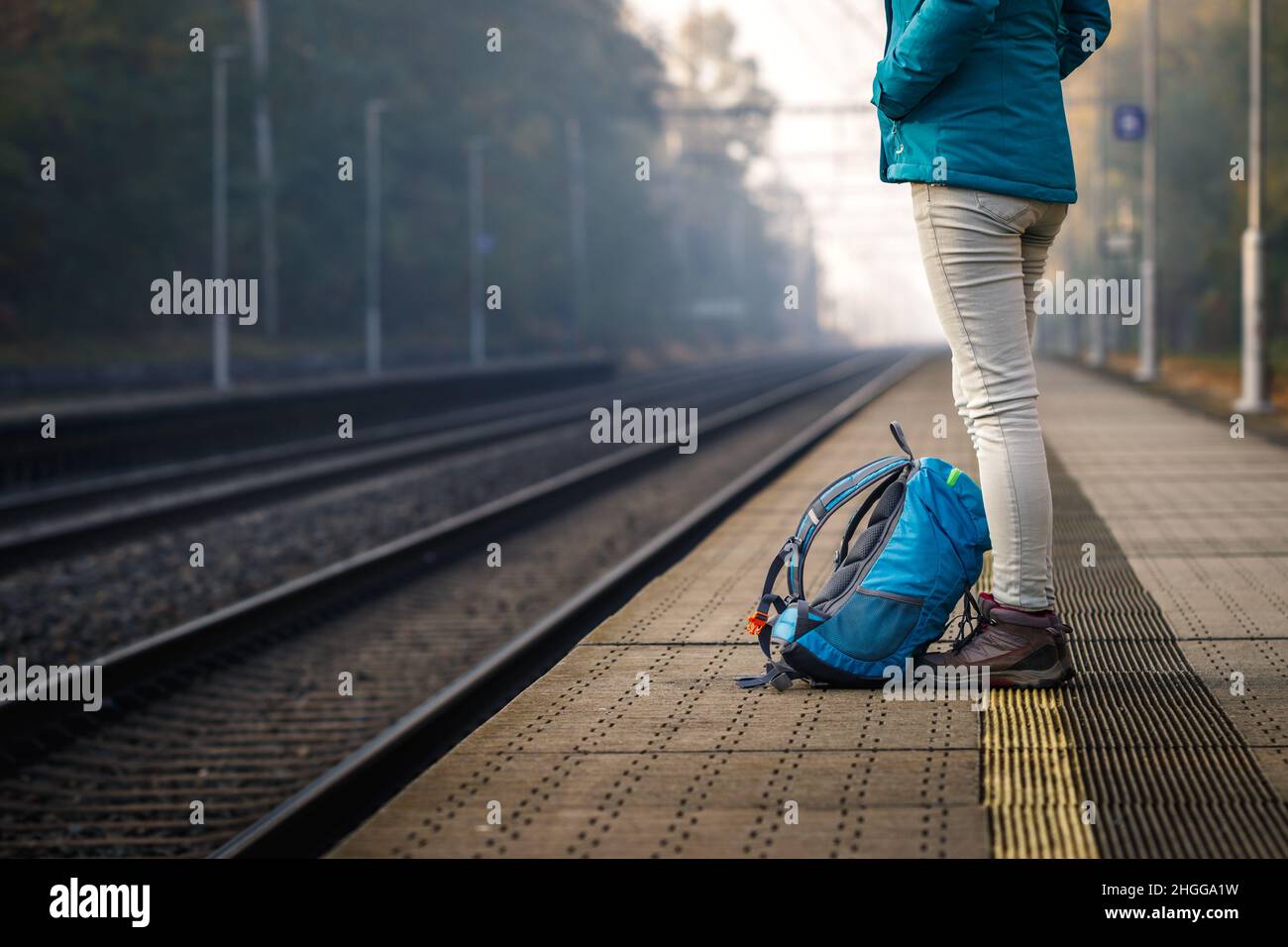 Alleinreisende, die am leeren Bahnhof auf den Zug warten. Frau mit Rucksack, die auf dem Bahnsteig steht Stockfoto