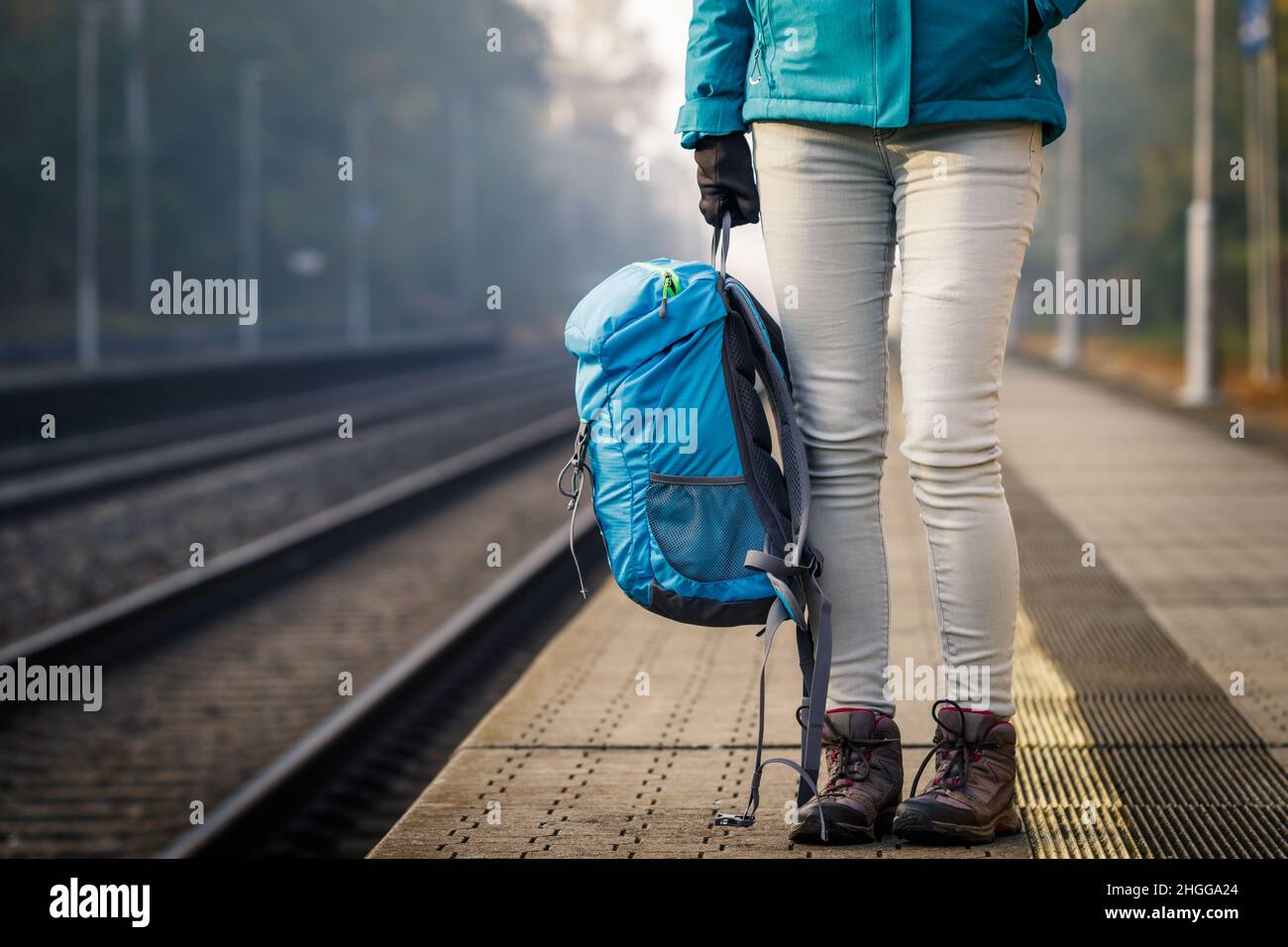 Alleinreisende, die am leeren Bahnhof auf den Zug warten. Frau mit Rucksack, die auf dem Bahnsteig steht Stockfoto