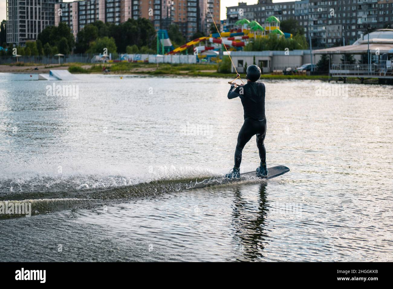 Sportlicher Mann, der am Wakeboard balanciert und am sonnigen Tag auf dem ruhigen Flusswasser reitet Stockfoto