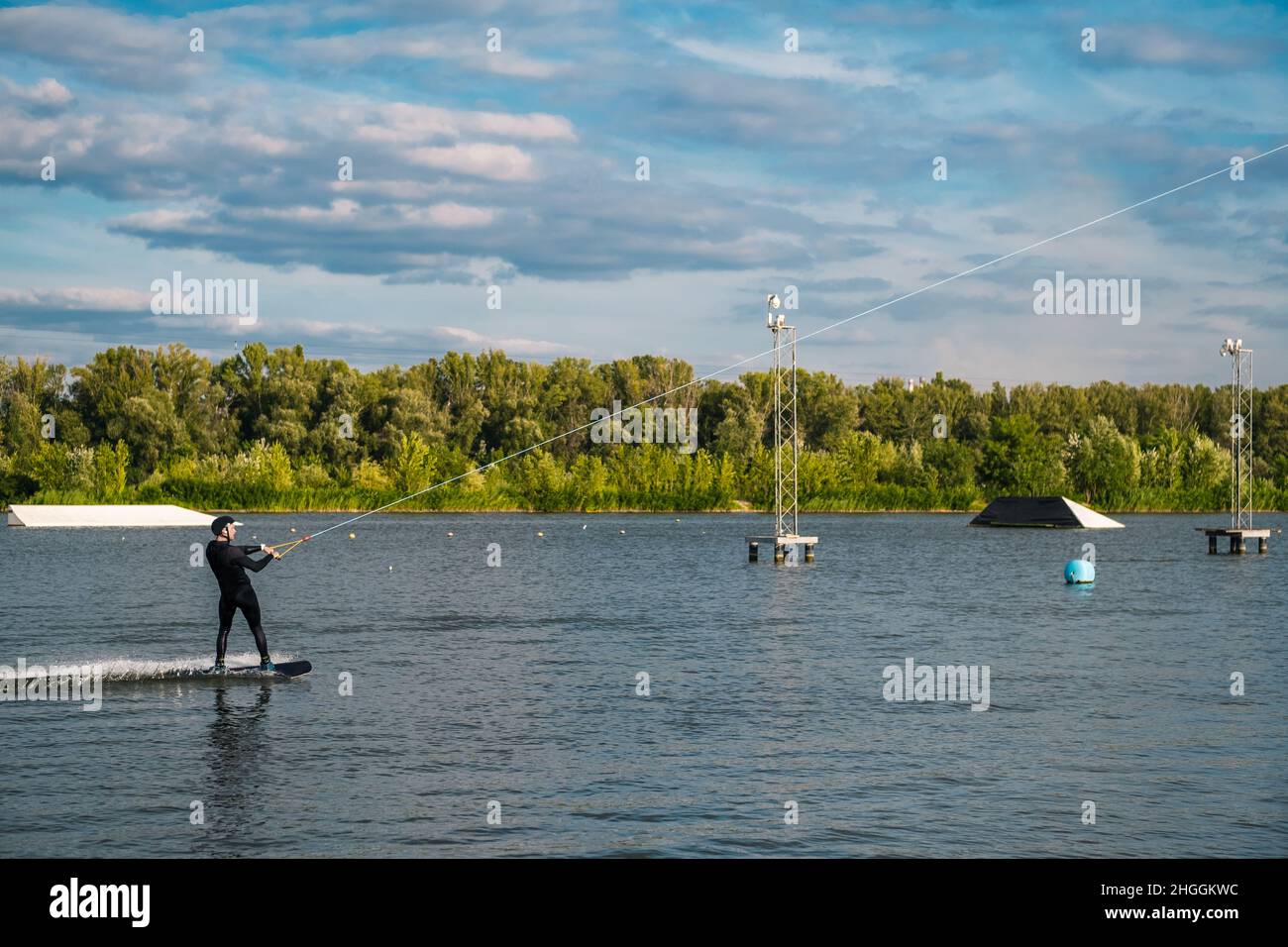 Fokussierter, sportlicher Mann, der auf dem Wakeboard auf dem Kabel auf dem ruhigen Fluss fährt Stockfoto