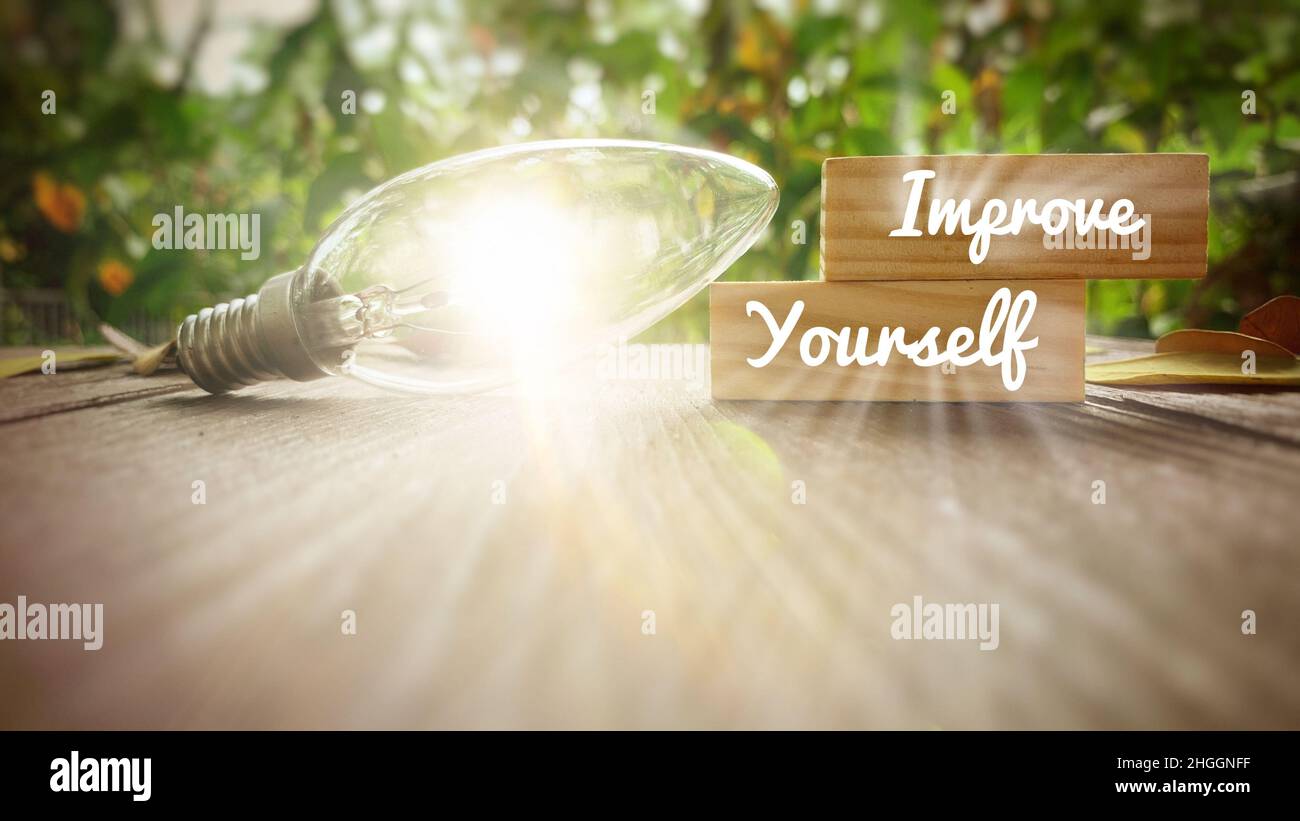 Verbessern Sie sich selbst Text auf Holzblöcke mit leuchtenden Glühbirne Hintergrund. Motivationskonzept. Stockfoto
