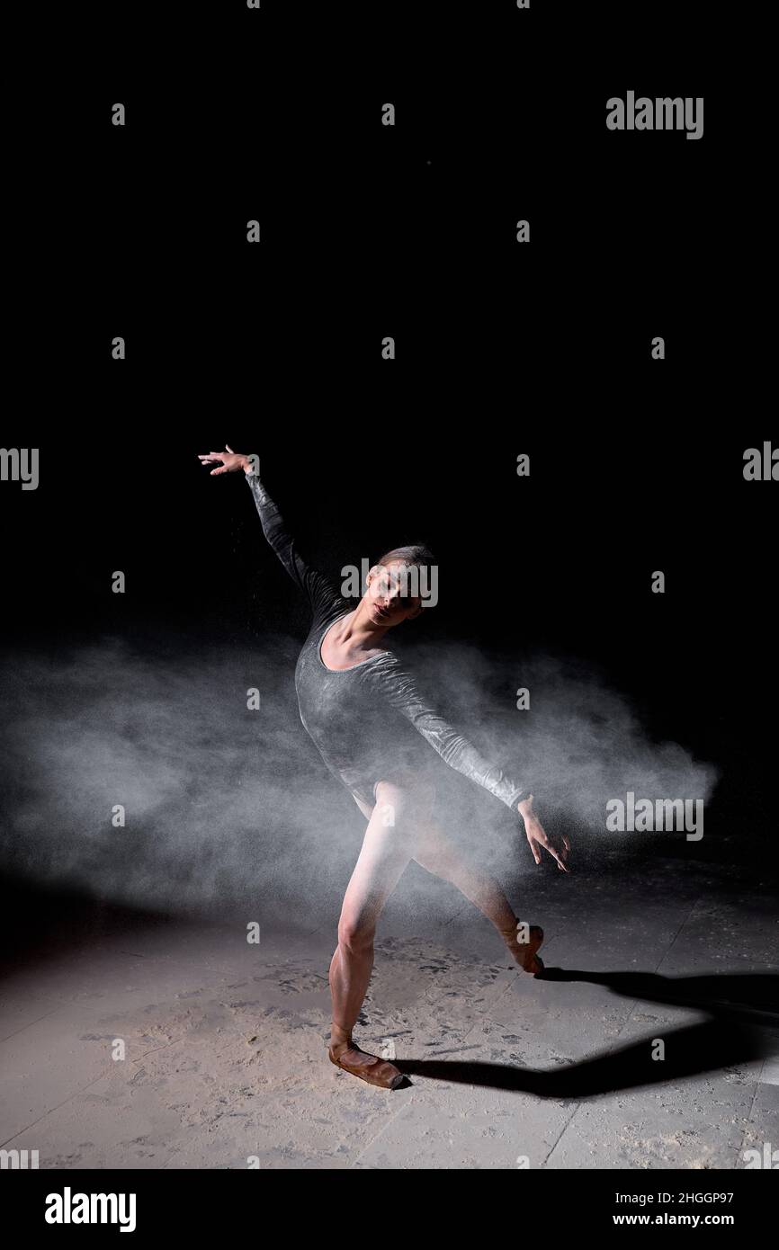 Schöne hübsche weibliche trägt schwarzen Gymnastikbodysuit tanzen mit fliegendem Pulvermehl, in voller Länge Porträt von attraktiven kaukasischen Dame in langsamen m Stockfoto