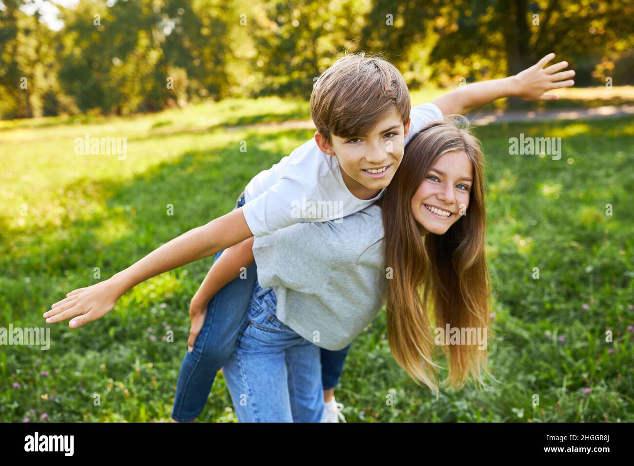 Schwester trägt ihren Bruder Huckepack, während sie im Sommer auf einer Wiese im Park spielt Stockfoto