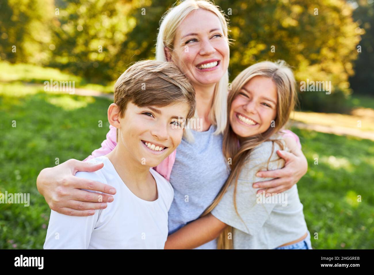 Im Sommer umarmt die glückliche Mutter ihre beiden Kinder liebevoll im Park Stockfoto