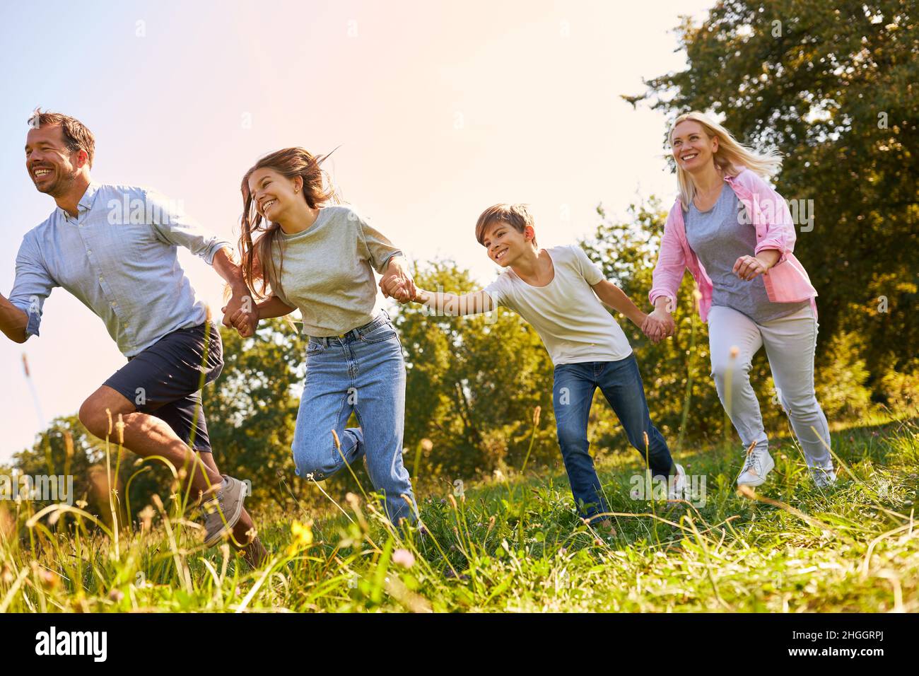 Sportliche Familie mit zwei Kindern hat im Sommer Spaß beim Laufen über eine Wiese Stockfoto