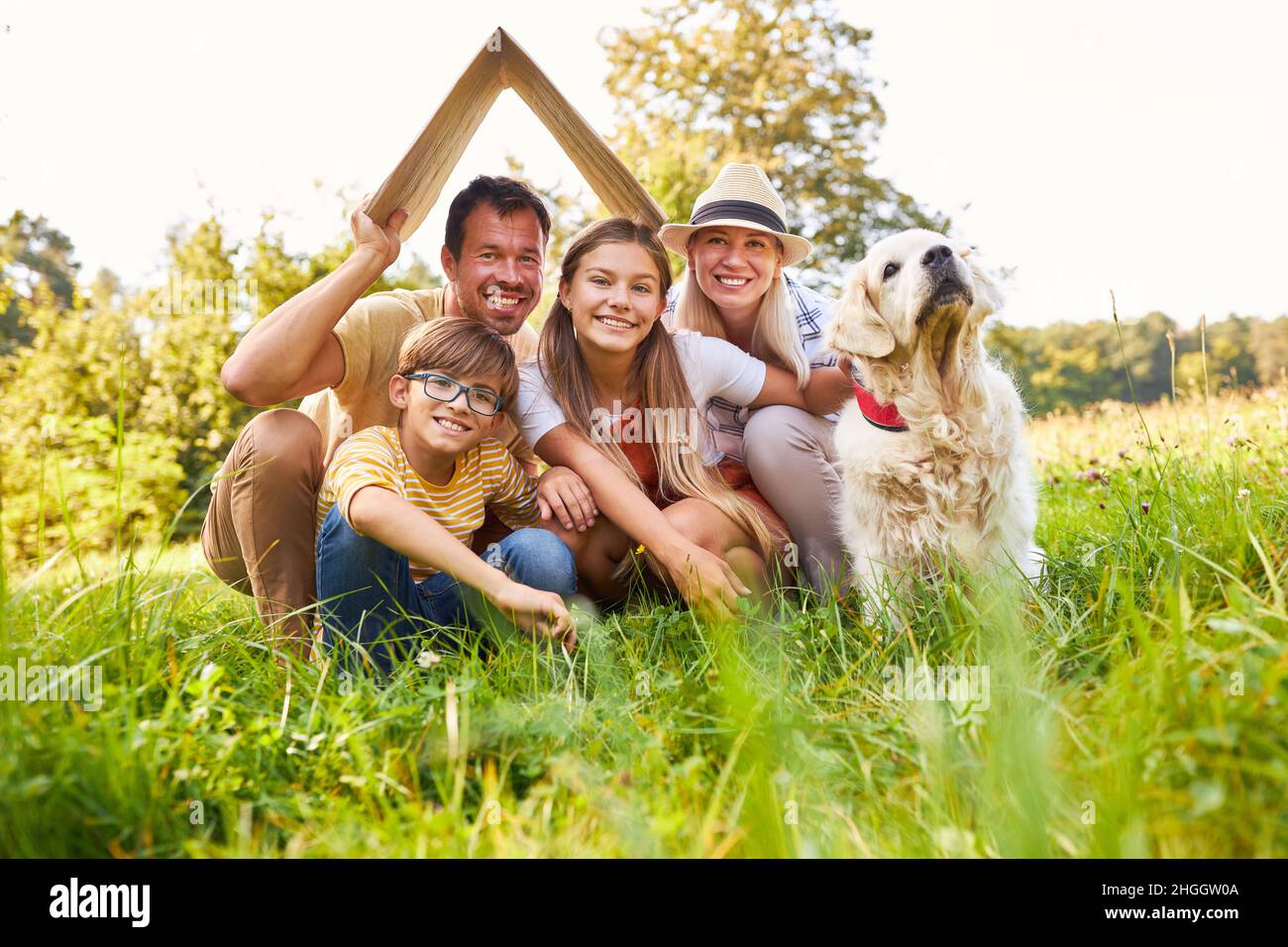 Glückliche kleine Familie und Hund mit einem Dach über dem Kopf als Symbol für den Bau oder Kauf eines Hauses Stockfoto