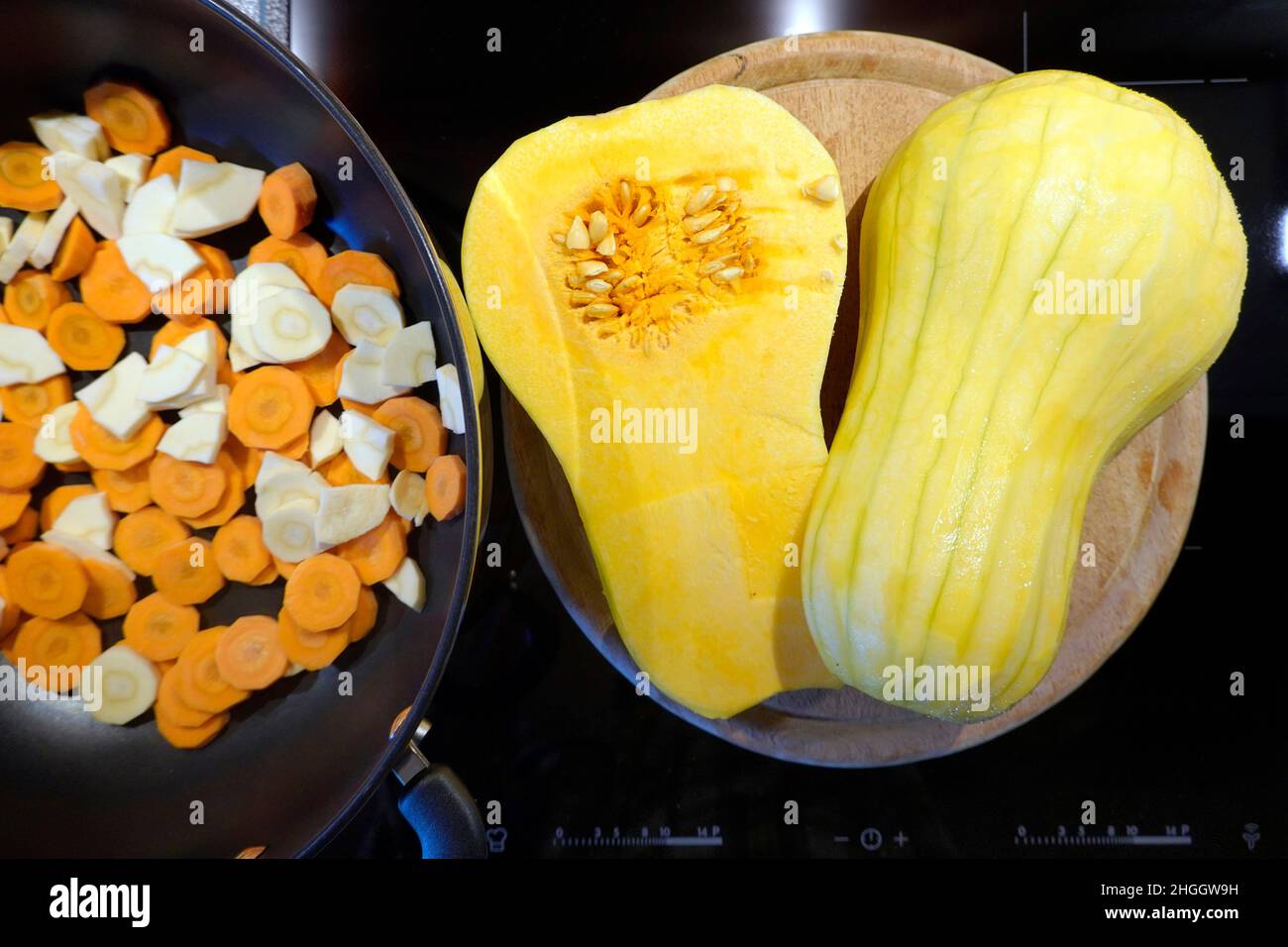 butternusskürbis (Cucurbita moschata), geschälter Butternusskürbis, in der Mitte geteilt, neben einer Pfanne mit Karotten und Pastinaken Stockfoto
